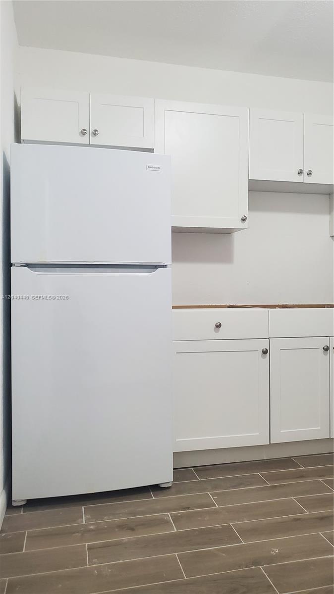 A white refrigerator stands next to white kitchen cabinets and drawers with wood-look tile flooring — 905 SW 4th Ter, Hallandale Beach FL 33009, HALLANDALE BEACH, FL