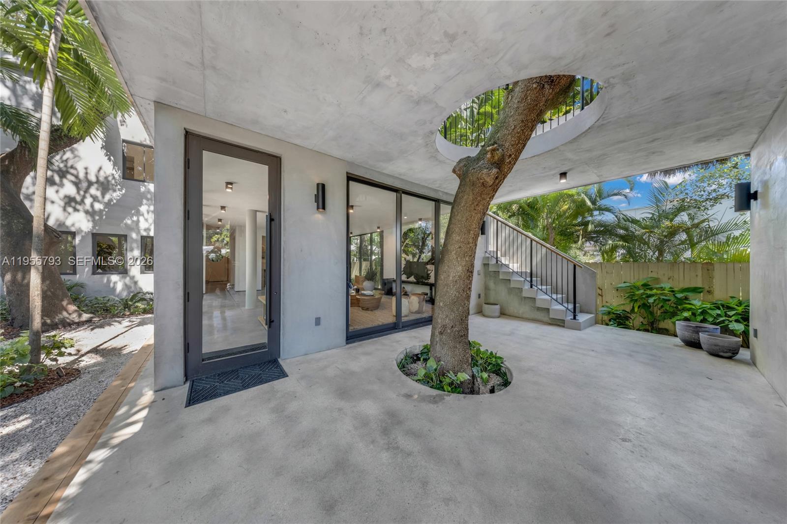 A concrete patio features a large tree growing through circular cutouts in the floor and ceiling — 1000 NW 9th Ct, Miami FL 33136, MIAMI, FL