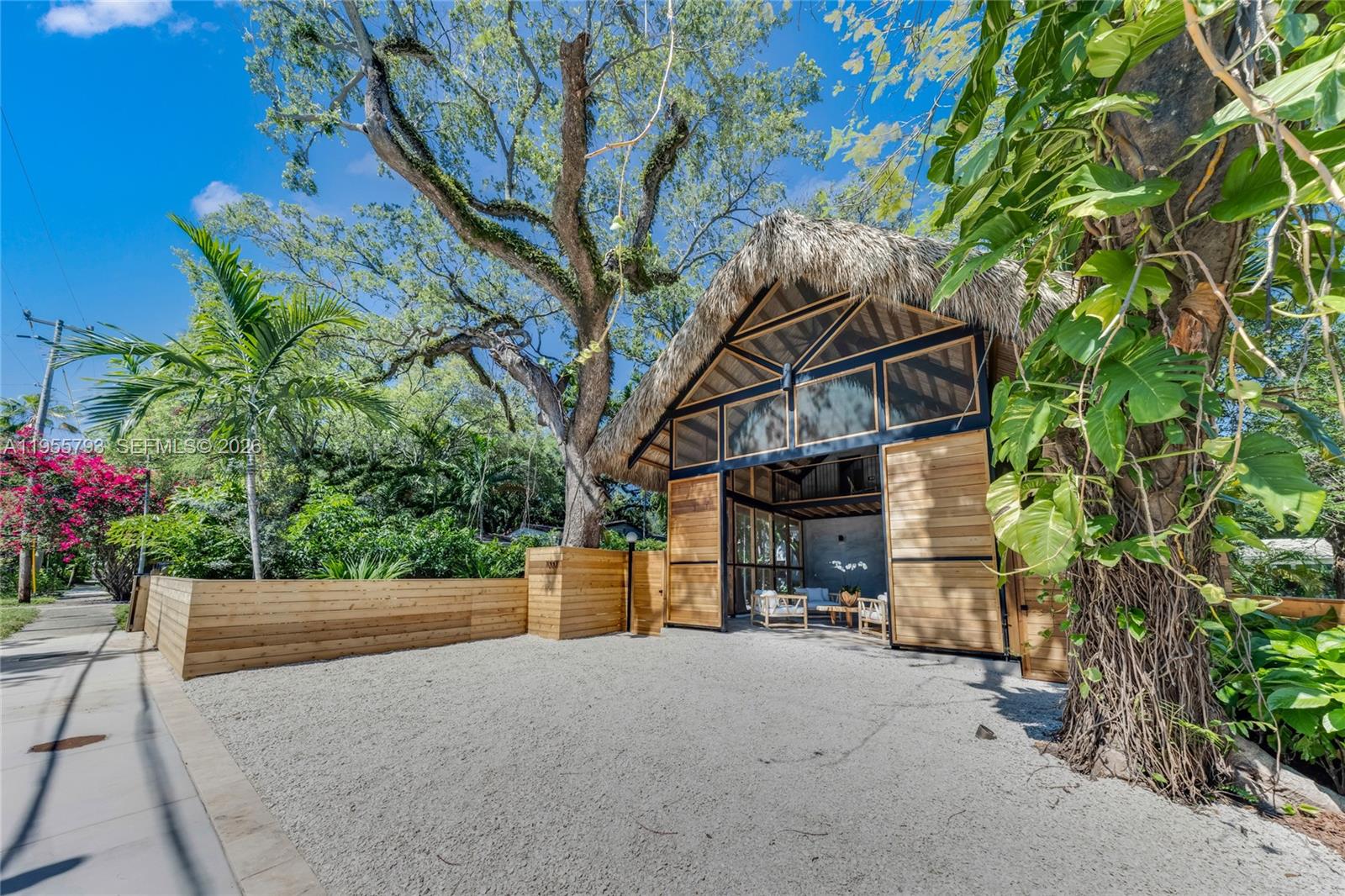 A thatched-roof structure with open wooden doors sits behind a gravel driveway and fence — 1000 NW 9th Ct, Miami FL 33136, MIAMI, FL