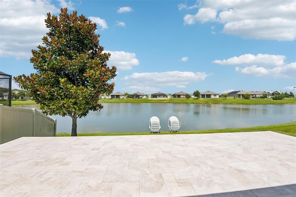 A paved patio overlooks a lake with two white chairs and a large magnolia tree — 7873 YALE HARBOR DRIVE, WESLEY CHAPEL, FL