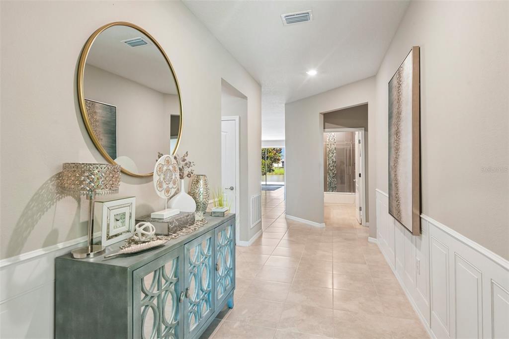 A hallway features a blue console table, a round mirror, and white wainscoting on walls — 7873 YALE HARBOR DRIVE, WESLEY CHAPEL, FL