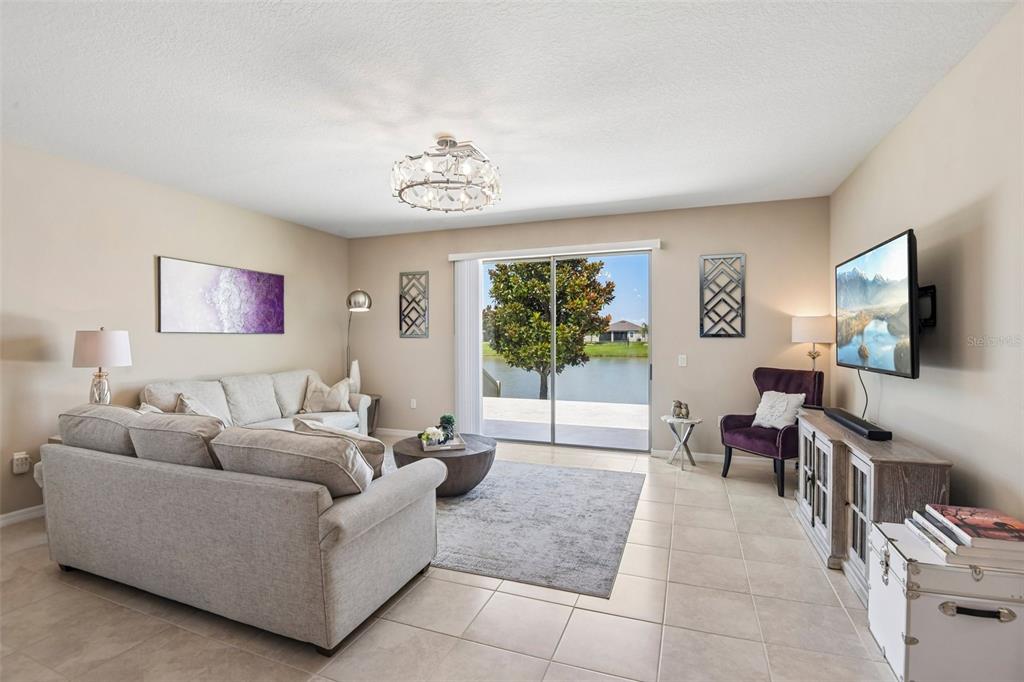 A living room features a beige sofa, a television, and a sliding door overlooking water — 7873 YALE HARBOR DRIVE, WESLEY CHAPEL, FL