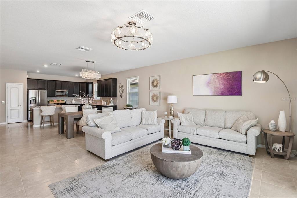 An open-concept living and dining area features neutral furniture, tile flooring, and dark kitchen cabinetry — 7873 YALE HARBOR DRIVE, WESLEY CHAPEL, FL