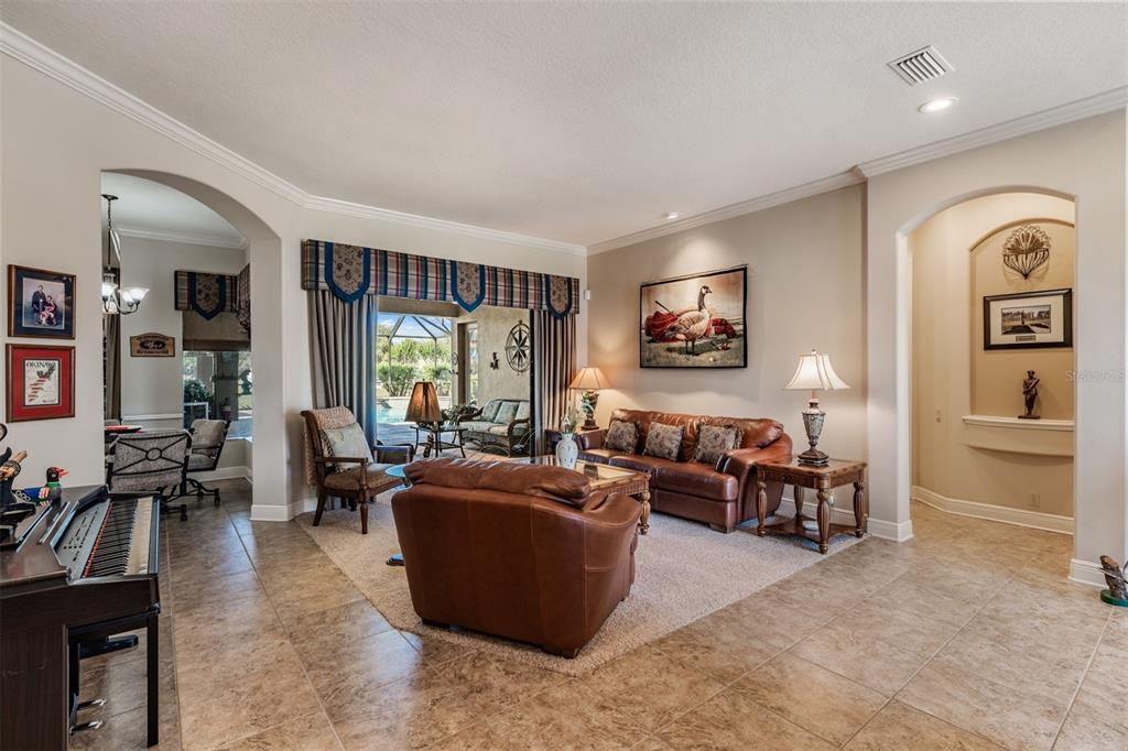 A living room with tile flooring, leather furniture, a piano, and a view of a pool — 34115 AMERICANA AVENUE, DADE CITY, FL