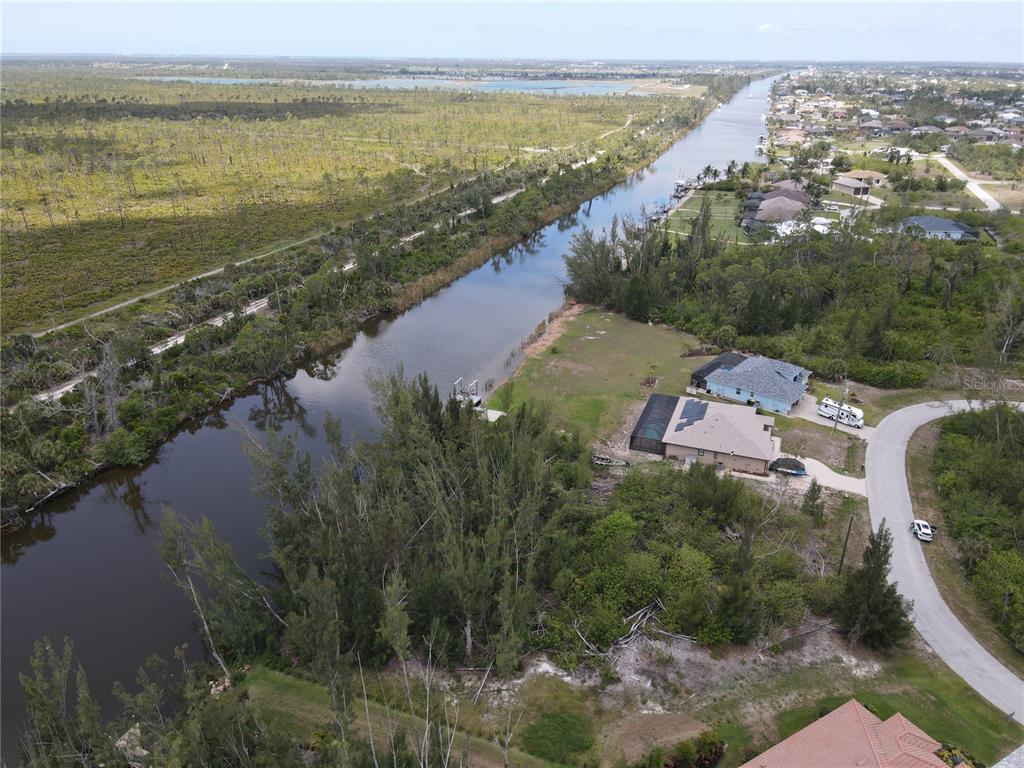 An aerial view shows a canal flowing past residential homes and a large wooded area — 10662 KEARSARGE CIRCLE, PORT CHARLOTTE, FL