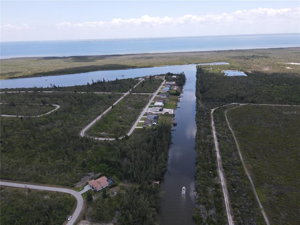 An aerial view shows a canal leading to a bay, surrounded by undeveloped land and houses — 10662 KEARSARGE CIRCLE, PORT CHARLOTTE, FL