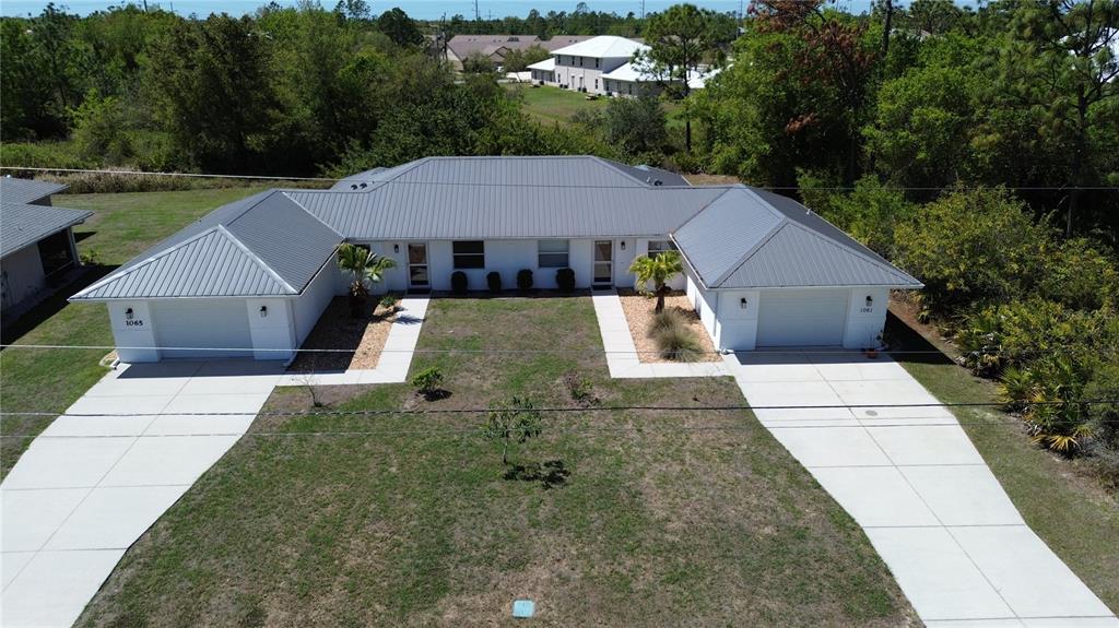 An aerial view shows a duplex with white walls, gray metal roofs, and concrete driveways — 1061+1065 NOMAD ROAD, PUNTA GORDA, FL