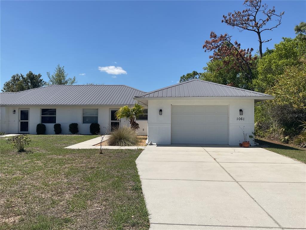 A white single-story house with a metal roof and an attached one-car garage — 1061+1065 NOMAD ROAD, PUNTA GORDA, FL