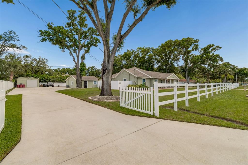 A concrete driveway leads to a house with a white fence and a detached garage — 9406 W FLORA STREET, TAMPA, FL