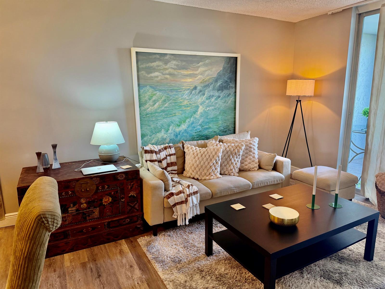 A living room features a beige sofa, a dark coffee table, and a large seascape painting — 14671 Bonaire Boulevard # 604, Delray Beach FL 33446, DELRAY BEACH, FL