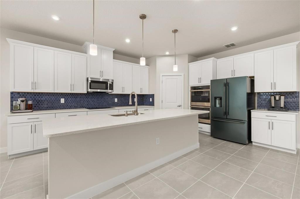 A modern kitchen features white cabinetry, a large quartz island, and a blue hexagonal backsplash — 11182 NELLIE CROSSING CIRCLE, CLERMONT, FL