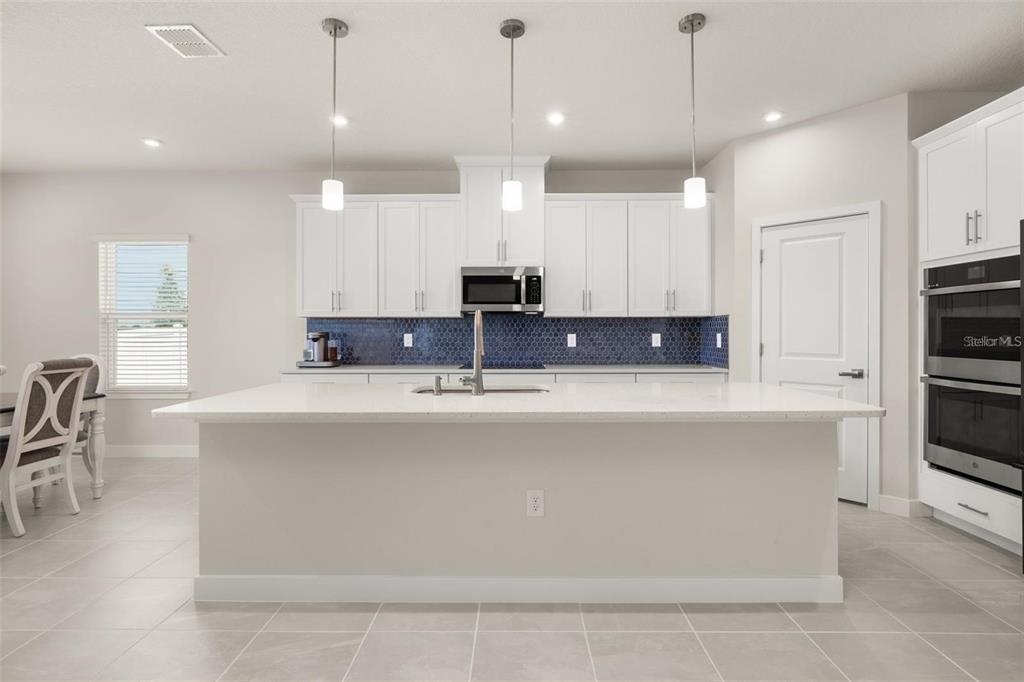 A modern kitchen features white cabinetry, a large quartz island, and a blue honeycomb backsplash — 11182 NELLIE CROSSING CIRCLE, CLERMONT, FL