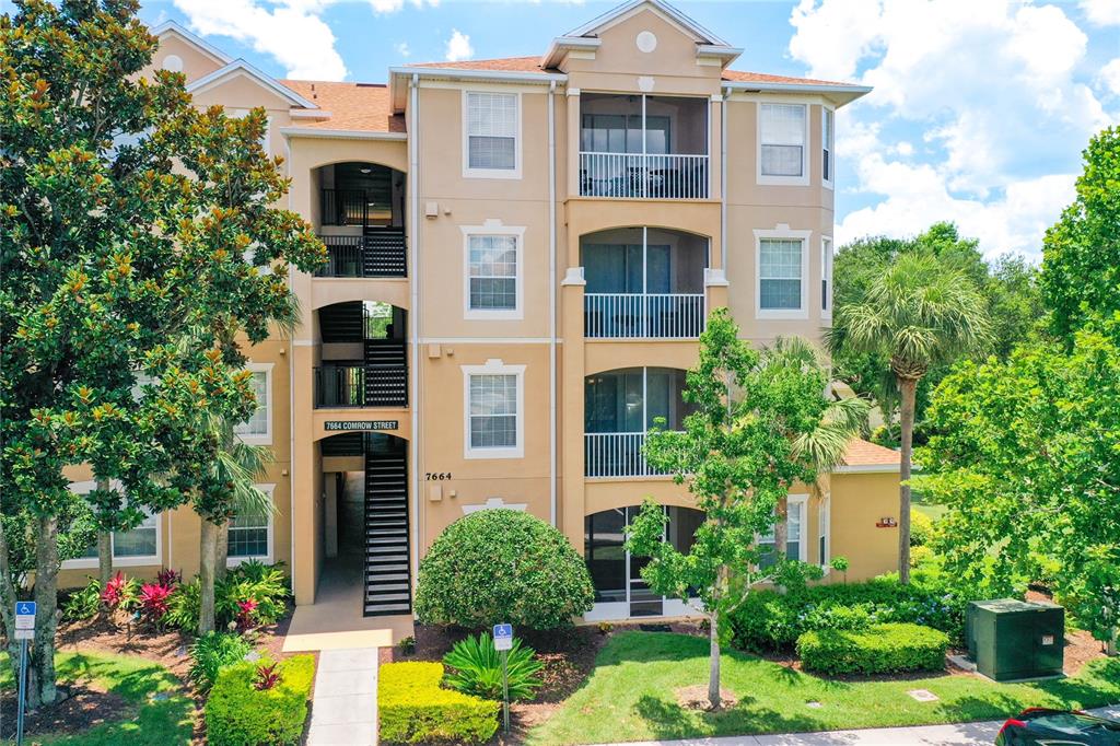 A three-story apartment building with tan stucco walls, screened balconies, and an exterior staircase — 7664 COMROW STREET UNIT 101, KISSIMMEE, FL