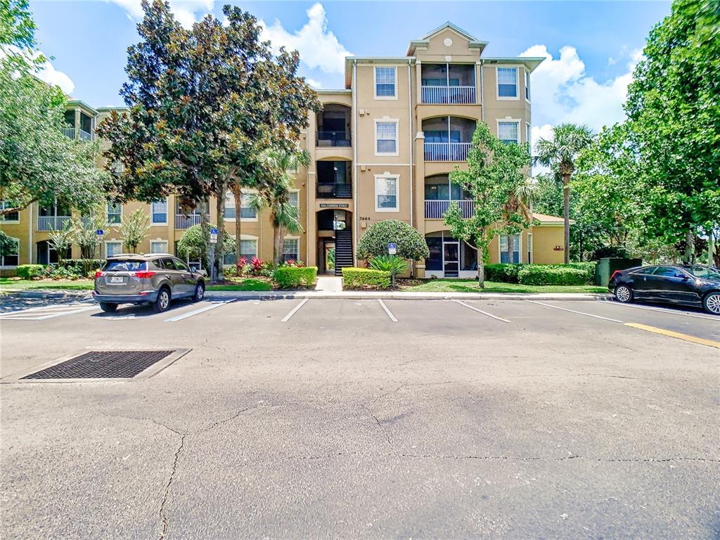 A multi-story apartment building with a parking lot in the foreground — 7664 COMROW STREET UNIT 101, KISSIMMEE, FL