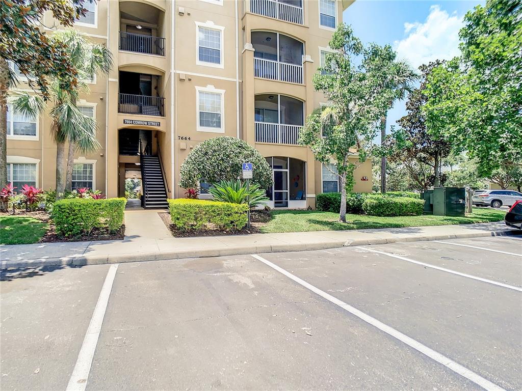 A multi-story apartment building exterior features a ground-level entrance, stairs, and a parking lot — 7664 COMROW STREET UNIT 101, KISSIMMEE, FL