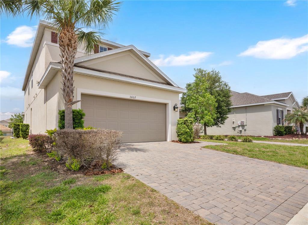 A two-story suburban house features a beige stucco exterior, a two-car garage, and a paver driveway — 3407 CURRENT AVENUE, WINTER GARDEN, FL