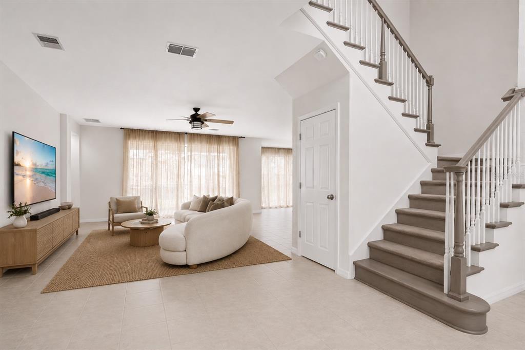 A living room with a curved sofa, television, and a staircase with grey wooden steps — 3407 CURRENT AVENUE, WINTER GARDEN, FL