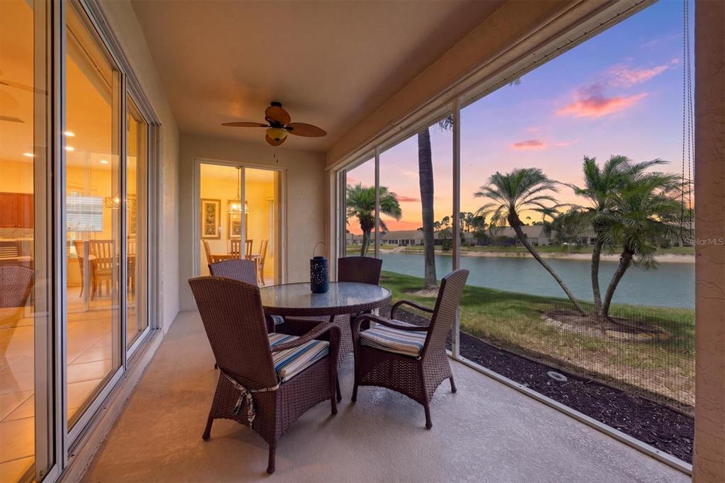 A screened-in patio features a dining set overlooking a lake at sunset — 445 TOMOKA DRIVE, ENGLEWOOD, FL