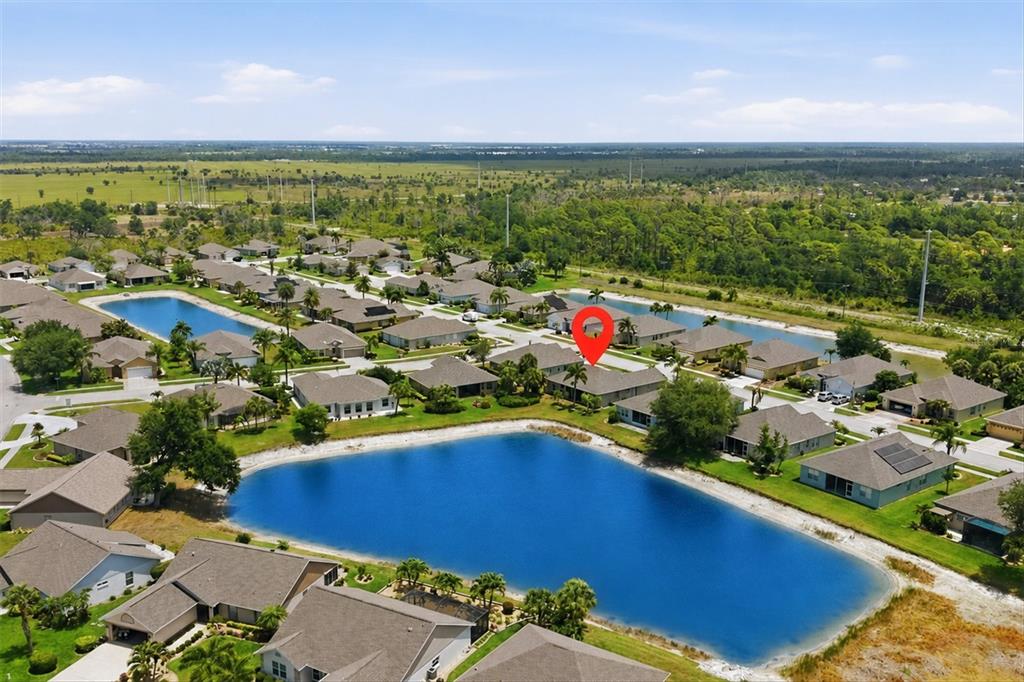 An aerial view of a suburban neighborhood featuring houses surrounding a large retention pond — 445 TOMOKA DRIVE, ENGLEWOOD, FL