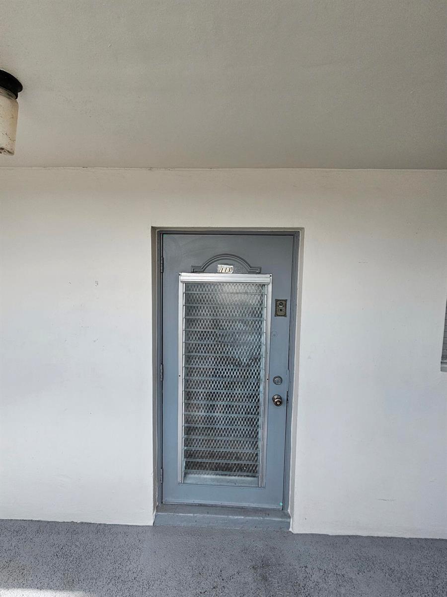 A gray exterior door with a security screen is set into a plain white wall — SUNRISE, FL