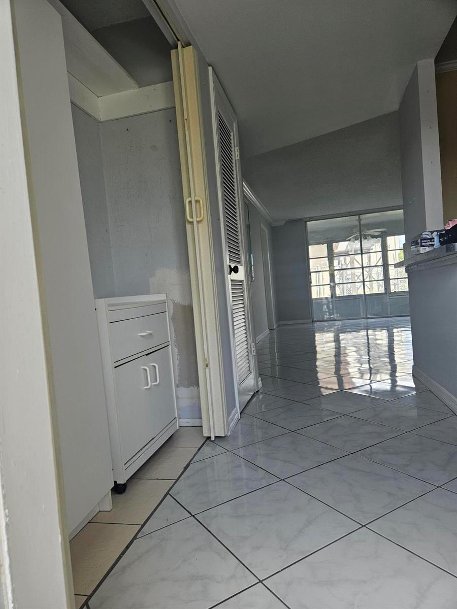 A hallway with light-colored tile flooring leads toward a glass-enclosed patio area — SUNRISE, FL