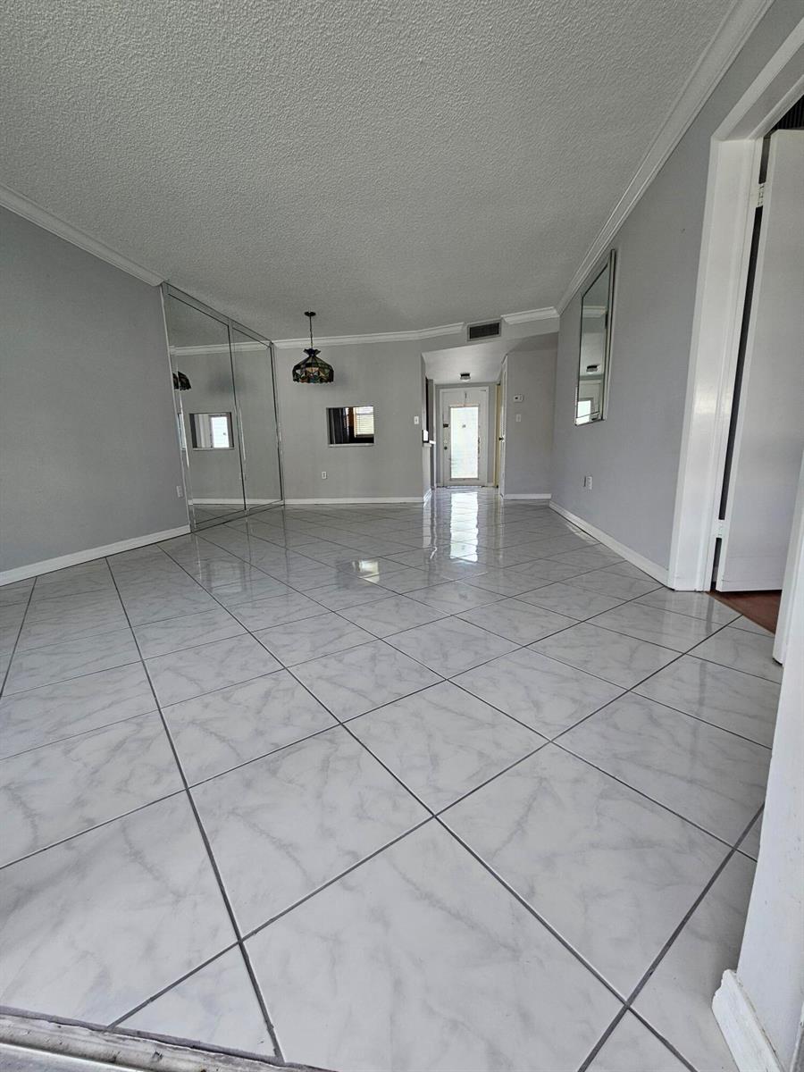 An empty room features light gray walls, white tile flooring, and a mirrored wall — SUNRISE, FL