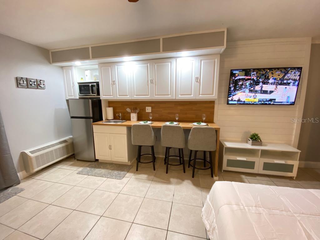 A kitchenette features white cabinets, a wood countertop, three bar stools, and a wall-mounted television — 1233 S ATLANTIC AVENUE UNIT 3160, DAYTONA BEACH, FL