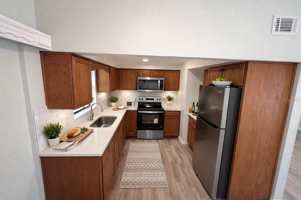 A kitchen with wood cabinets, stainless steel appliances, white countertops, and a subway tile backsplash — 3823 PINE RIDGE ROAD, ORLANDO, FL