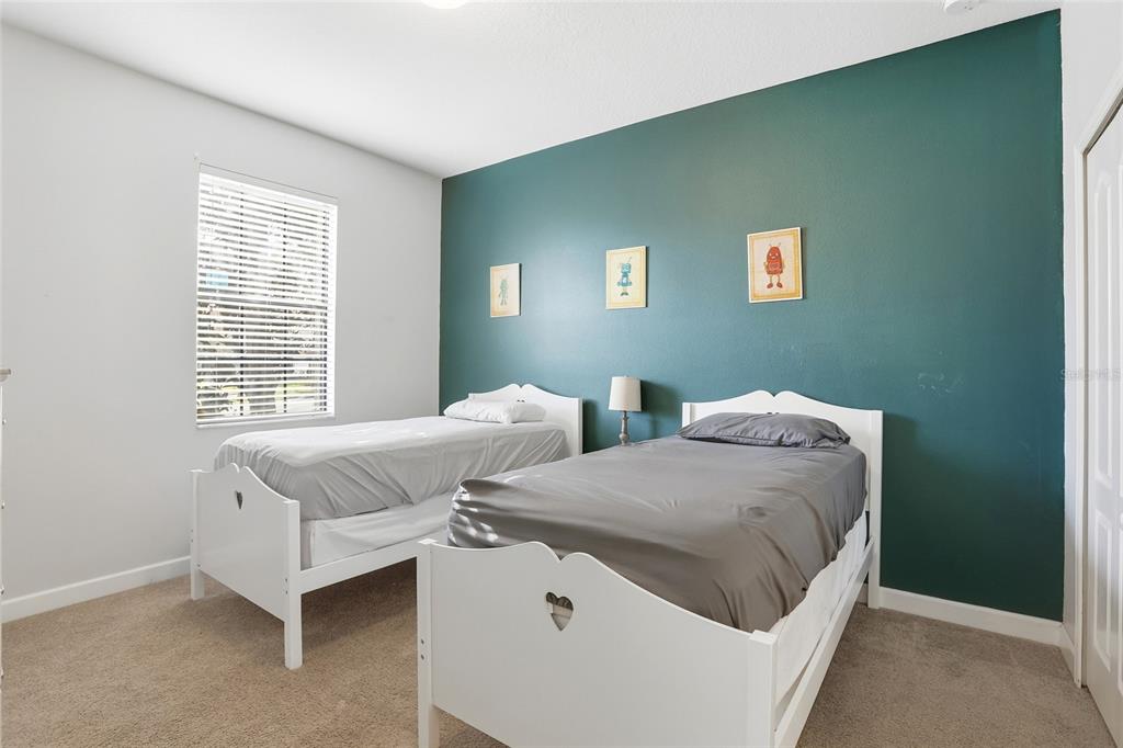 A bedroom features two white twin beds against a teal accent wall with three pictures — 9039 SHADOW MOUNTAIN STREET, DAVENPORT, FL