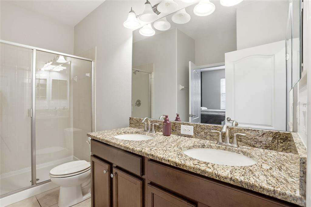 A bathroom with a double-sink granite vanity, dark wood cabinets, and a glass-enclosed shower — 9039 SHADOW MOUNTAIN STREET, DAVENPORT, FL