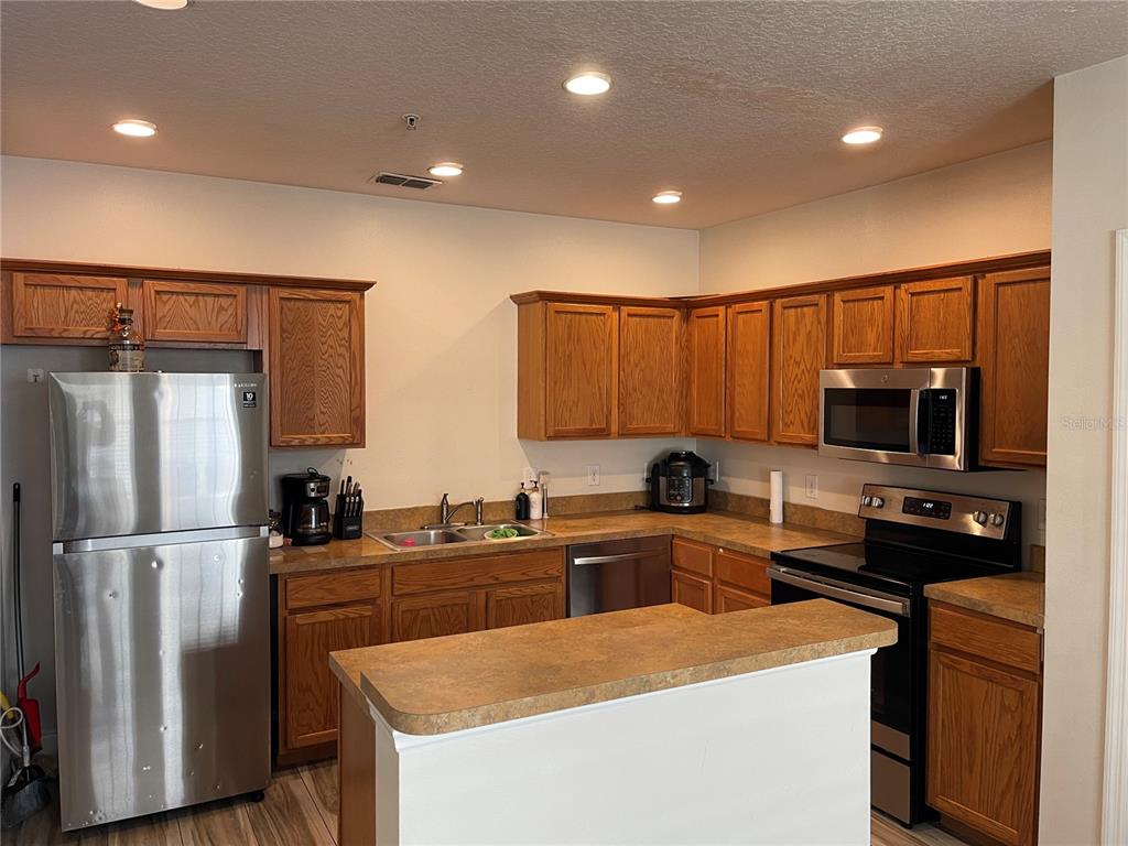 A kitchen features oak cabinets, stainless steel appliances, and a peninsula countertop — 2024 CYPRESS BAY BOULEVARD, KISSIMMEE, FL