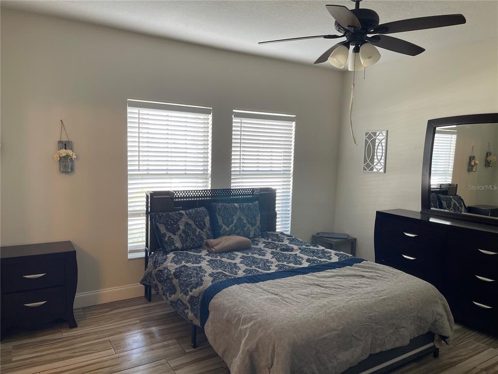 A bedroom features a bed with blue patterned bedding, dark wood furniture, and wood-look flooring — 2024 CYPRESS BAY BOULEVARD, KISSIMMEE, FL
