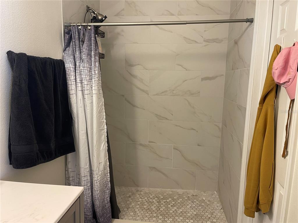 A tiled walk-in shower features a patterned curtain, marble-look wall tiles, and a pebble floor — 2024 CYPRESS BAY BOULEVARD, KISSIMMEE, FL