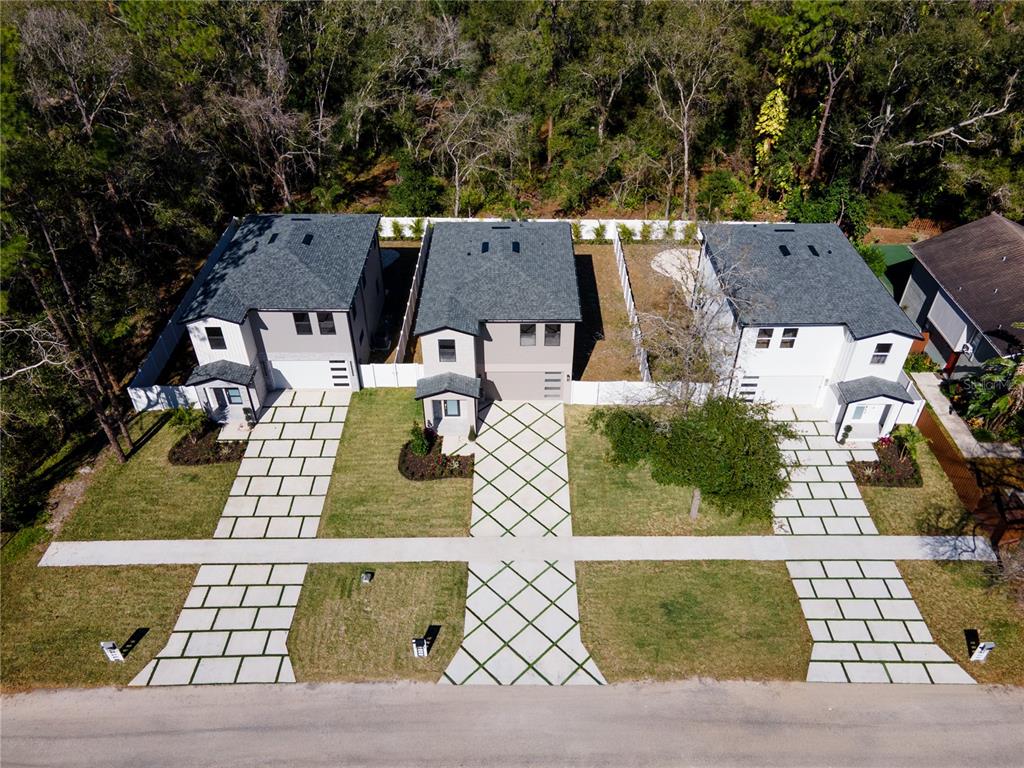 An aerial view shows three modern houses with paved driveways and walkways in a wooded area — 7617 AMHERST STREET, TAMPA, FL