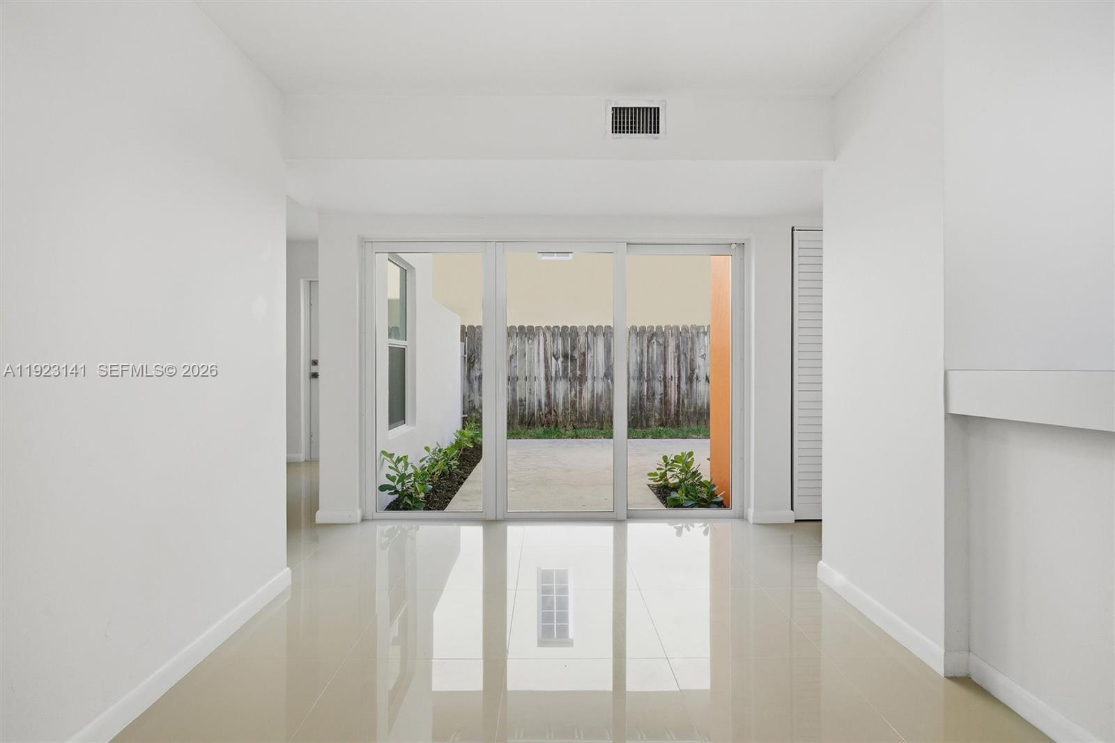 A bright room with white walls and glossy tile flooring leads to a glass sliding door — 1045 SW 25th Ave, Miami FL 33135, MIAMI, FL