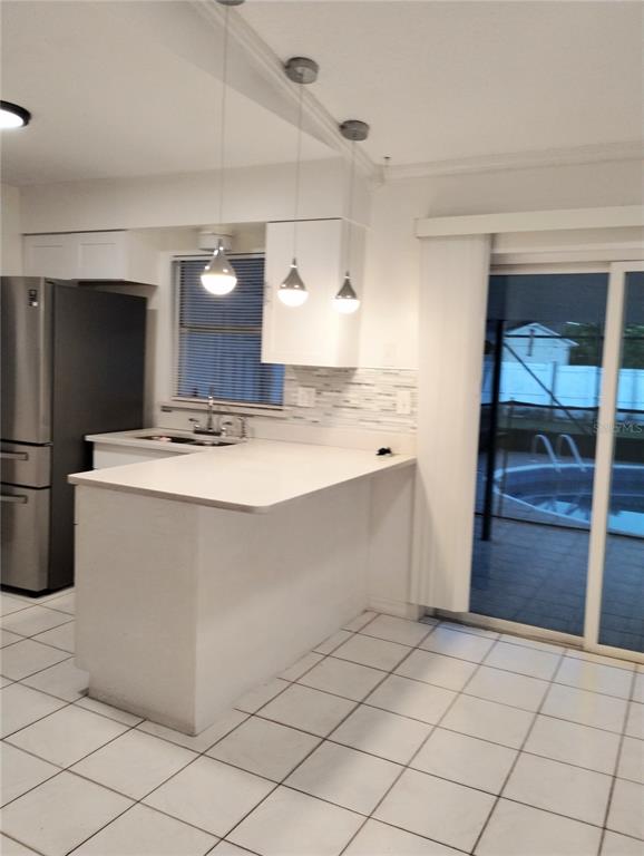 A kitchen with a white breakfast bar, stainless steel refrigerator, and sliding glass patio doors — 708 ANTELOPE WAY, KISSIMMEE, FL