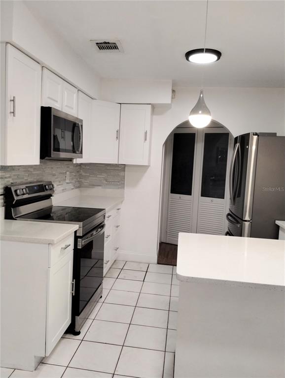 A kitchen features white cabinets, stainless steel appliances, a tile backsplash, and white tiled floors — 708 ANTELOPE WAY, KISSIMMEE, FL
