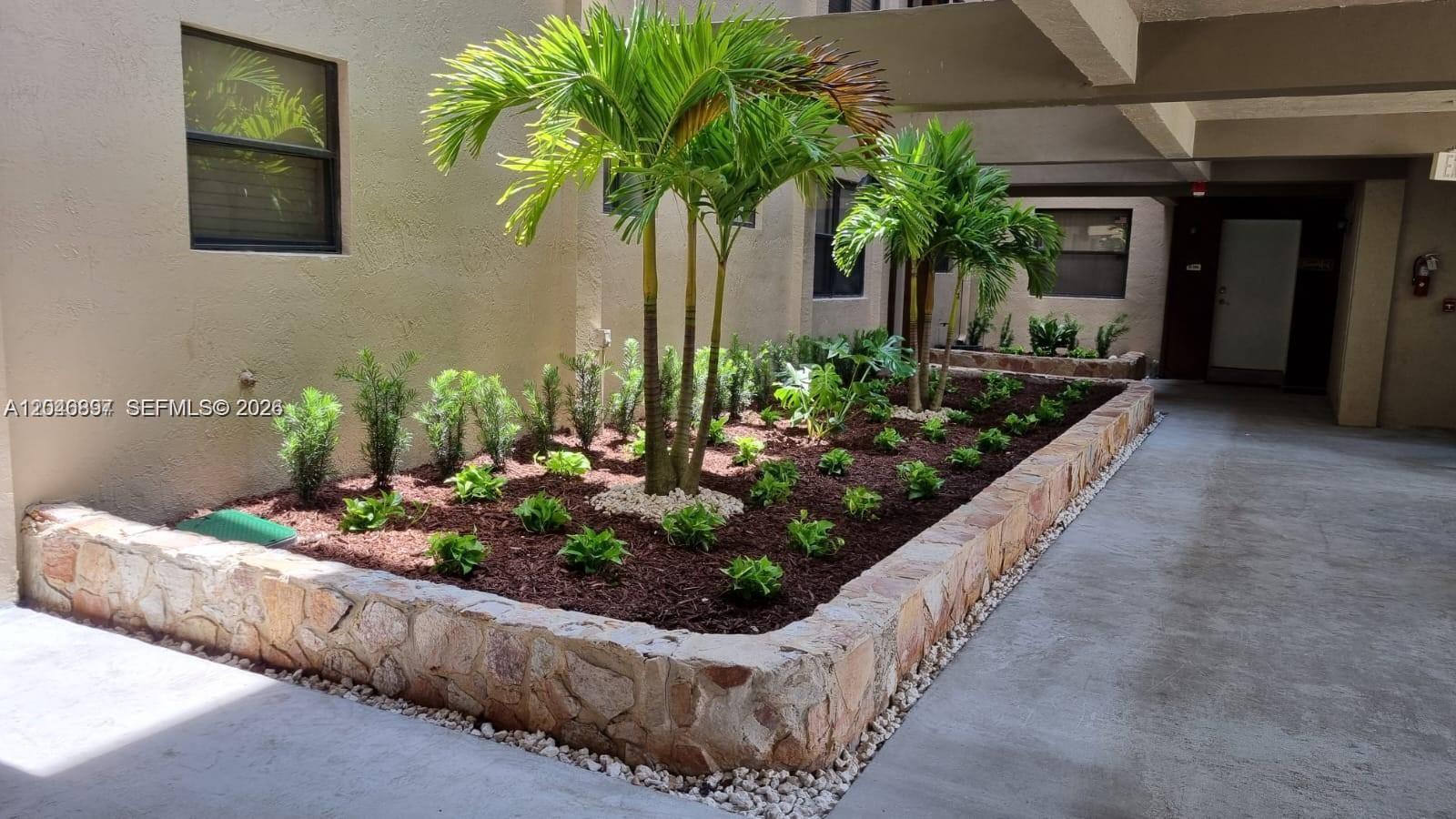 A stone-walled garden bed features palm trees and small shrubs in a building courtyard — 461 Ives Dairy Rd # 2, Miami FL 33179, MIAMI, FL