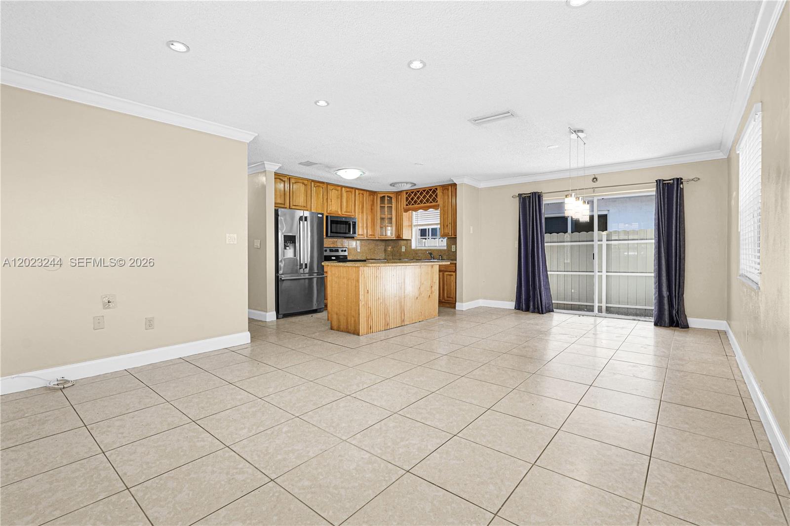 This open-concept kitchen and dining area features tile flooring, wood cabinetry, and sliding glass doors — 2400 SW 103rd Ct, Miami FL 33165, MIAMI, FL