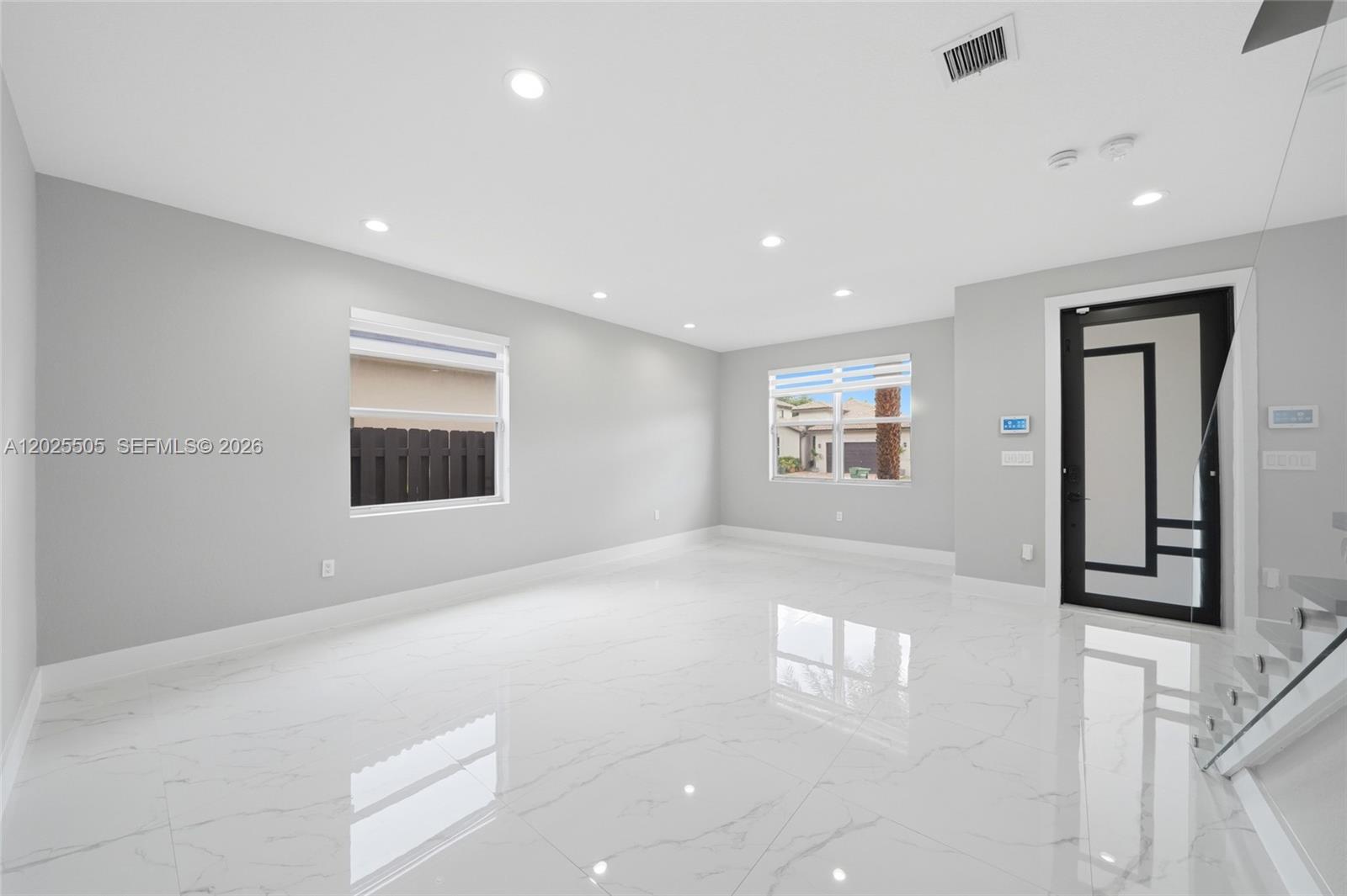 A bright, empty room features white marble-look tile flooring, light gray walls, and a modern door — 4107 NE 20th St, Homestead FL 33033, HOMESTEAD, FL