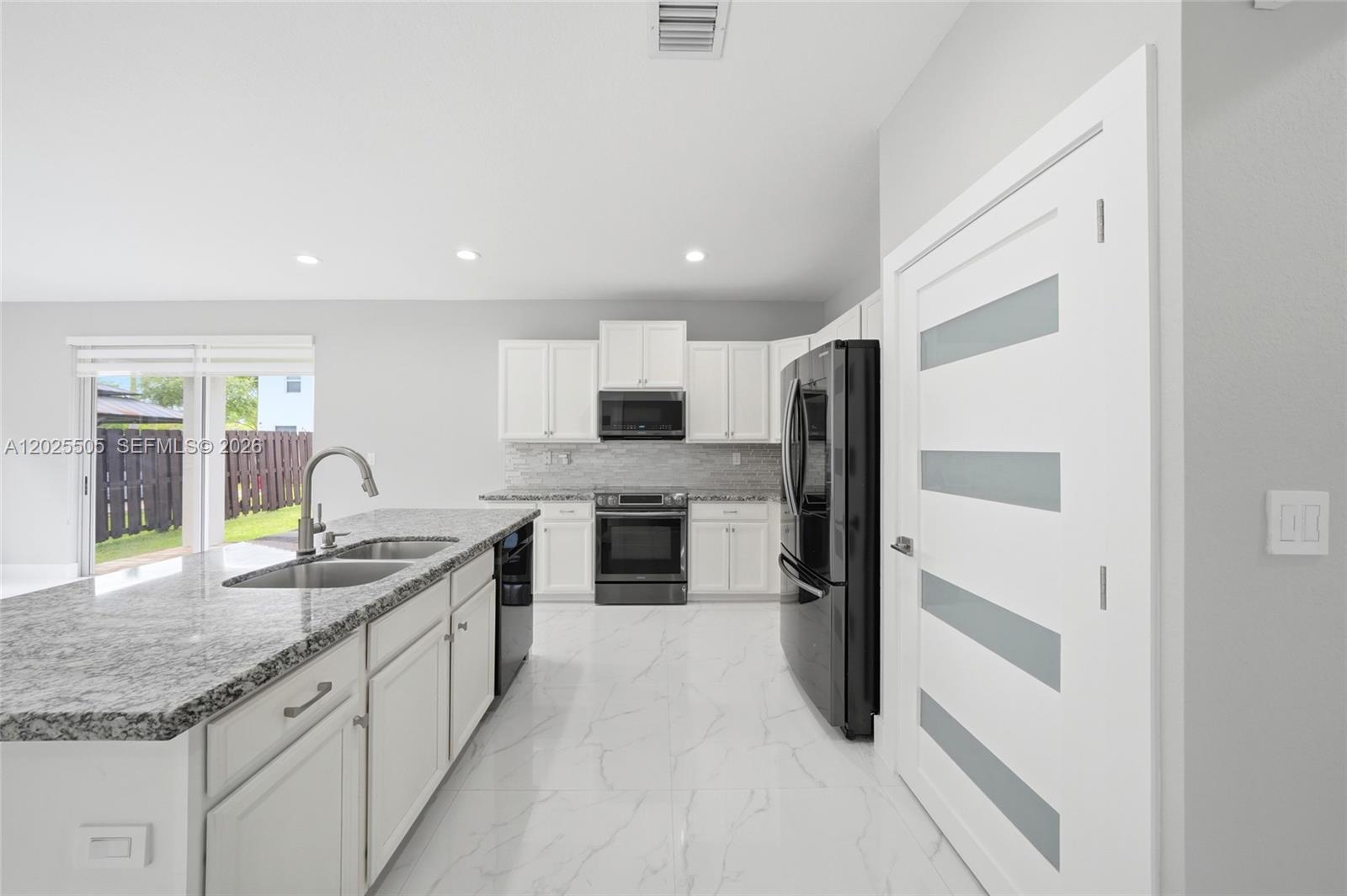 A modern kitchen features white cabinetry, granite countertops, black appliances, and white marble-look tile flooring — 4107 NE 20th St, Homestead FL 33033, HOMESTEAD, FL