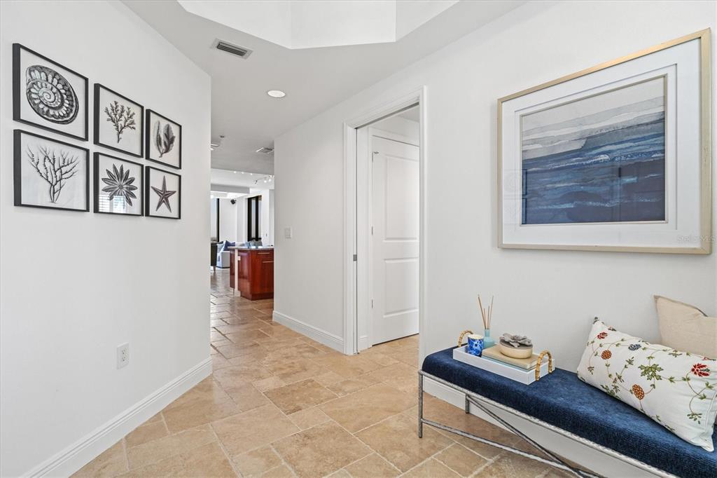 A hallway with tile flooring, a blue bench, and framed wall art leads to a kitchen — 50 CENTRAL AVENUE UNIT 15A, SARASOTA, FL