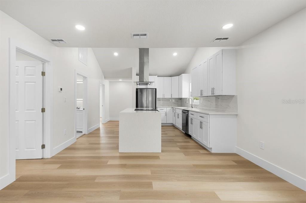 A modern kitchen features white cabinetry, a central island, and light wood-look flooring — 2590 18TH AVENUE N, ST PETERSBURG, FL