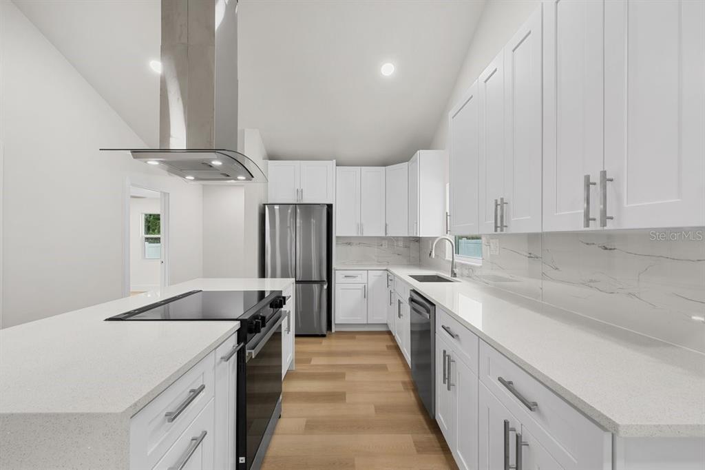 A modern kitchen features white cabinetry, quartz countertops, stainless steel appliances, and wood-look flooring — 2590 18TH AVENUE N, ST PETERSBURG, FL