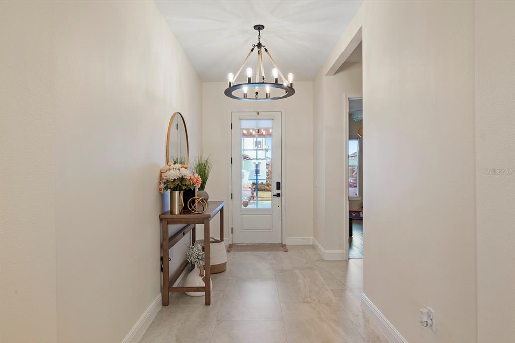 A bright entryway features a wooden console table, a chandelier, and light-colored tile flooring — 13301 MCMILLAN DRIVE, ORLANDO, FL