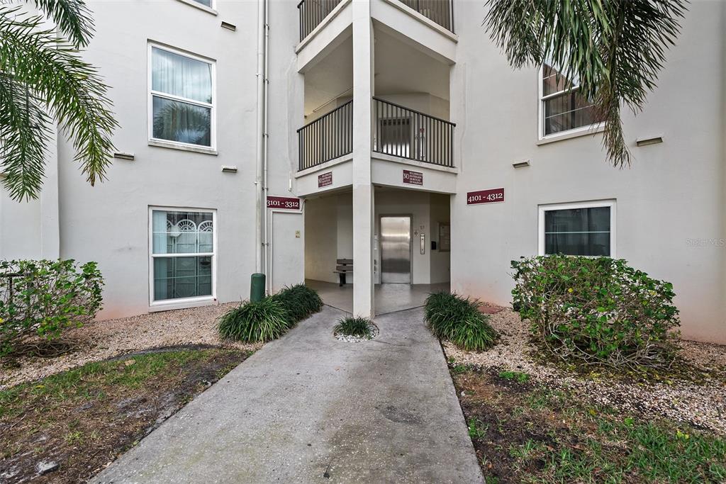 A concrete walkway leads to an elevator entrance between two sections of a residential building — 2700 BAYSHORE BOULEVARD UNIT 4106, DUNEDIN, FL