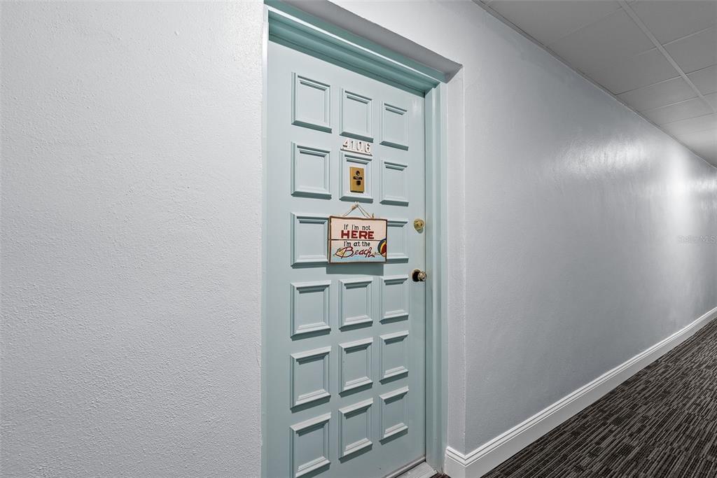 A light blue door with a beach-themed sign is located in a carpeted apartment hallway — 2700 BAYSHORE BOULEVARD UNIT 4106, DUNEDIN, FL