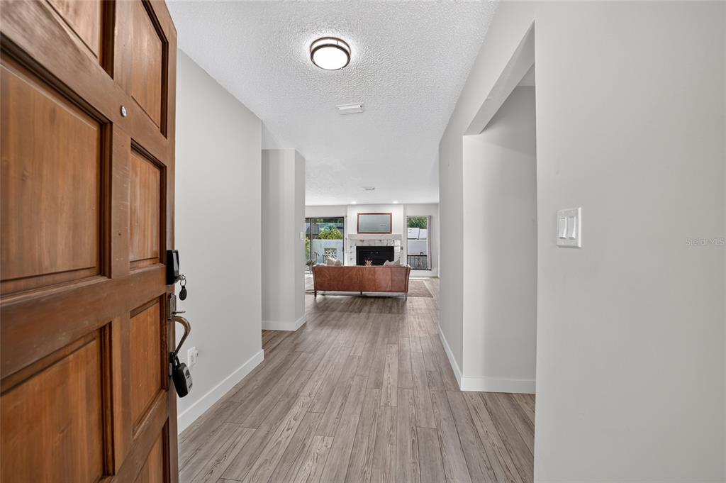 A view from an open wooden front door into a hallway with light wood flooring — 3867 NE 17TH STREET CIRCLE, OCALA, FL