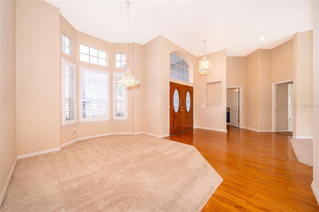 A dining area with beige carpet and a chandelier sits next to a hardwood foyer — 2277 NECTAR WAY, OVIEDO, FL