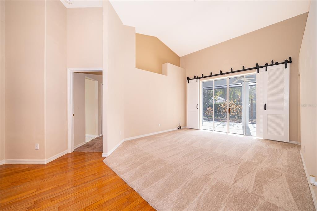 A room with vaulted ceilings, beige carpet, hardwood flooring, and sliding glass doors to a patio — 2277 NECTAR WAY, OVIEDO, FL